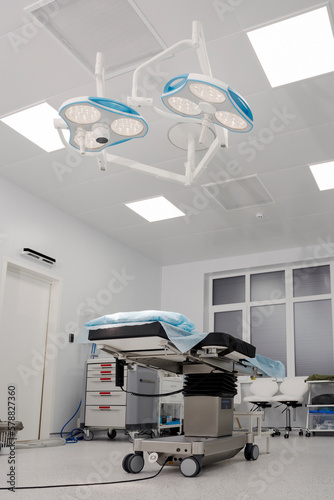 Spacious, well-equipped operating room, in the center of which there is an operating table, and an operating lamp is directed to it. The concept of health care, saving life. © speed300