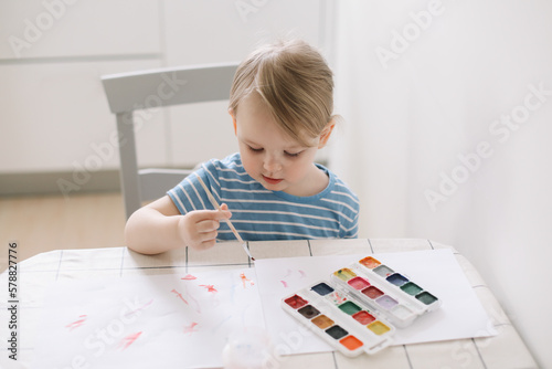 Child painting and drawing with watercolor paint at white table. Development of creative potential in children. quarantine, homeschooling concept