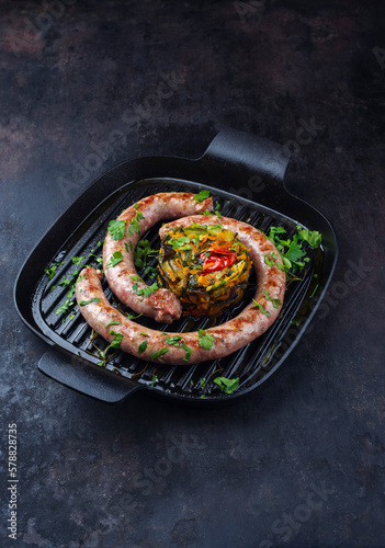 Traditionell gebratene italienische Fleischwurst Salsiccia fresco mit Gemüsetartar und Koriander serviert als close-up in einer gusseisernen Pfanne  photo