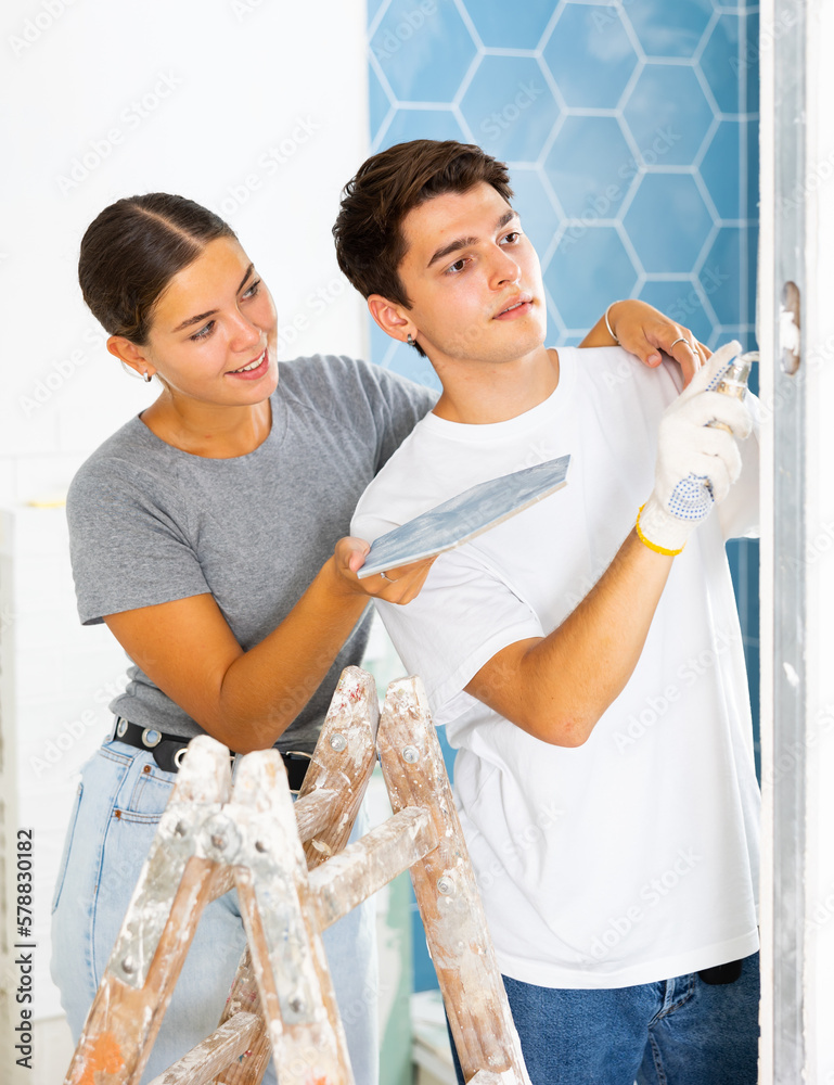Fototapeta premium Happy young couple doing repairs in the bathroom glues ceramic tiles on the wall