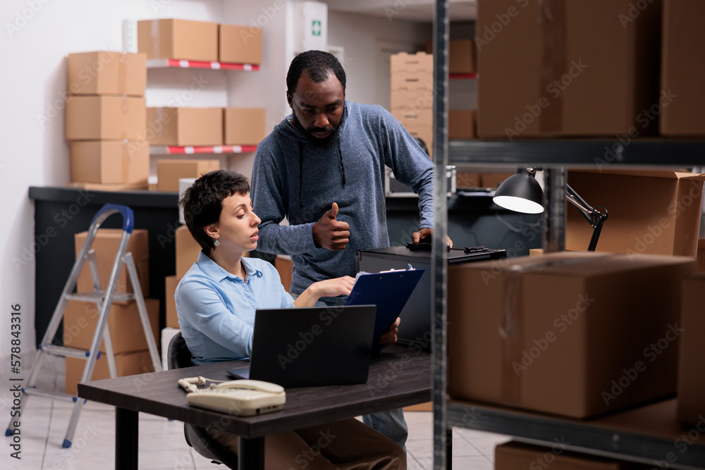 Supervisor woman analyzing metallic delivery order on clipboard discussing transportation logistics with worker while working together in warehouse. Storehouse team checking distribution stock Supervisor woman analyzing metallic delivery order on clipboard discussing transportation logistics with worker while working together in warehouse. Storehouse team checking distribution stock