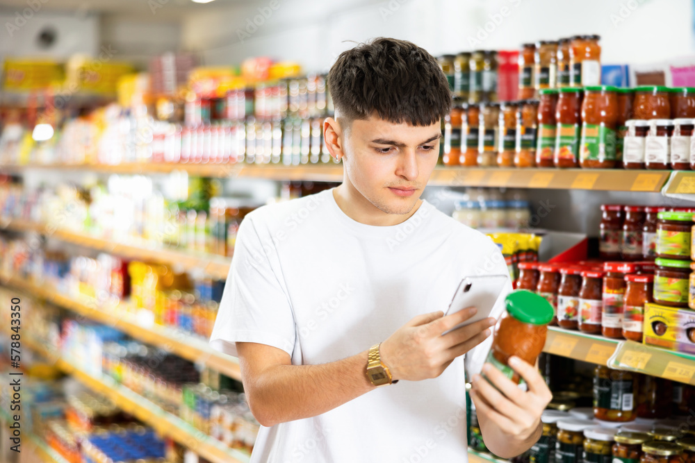 Young man looking up contents of preserved food on internet in supermarket