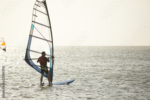 Windsurfer against the backdrop of the setting sun, on calm water, goes calmly along the sea, active recreation, copyspace.