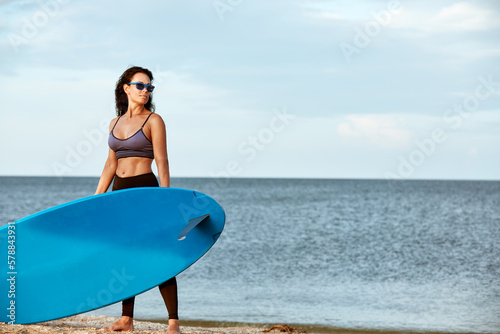 Photography Sexy middle aged brunette with a surfboard in the setting sun holds a surfboard on her head, surfing as a lifestyle, waiting for the waves