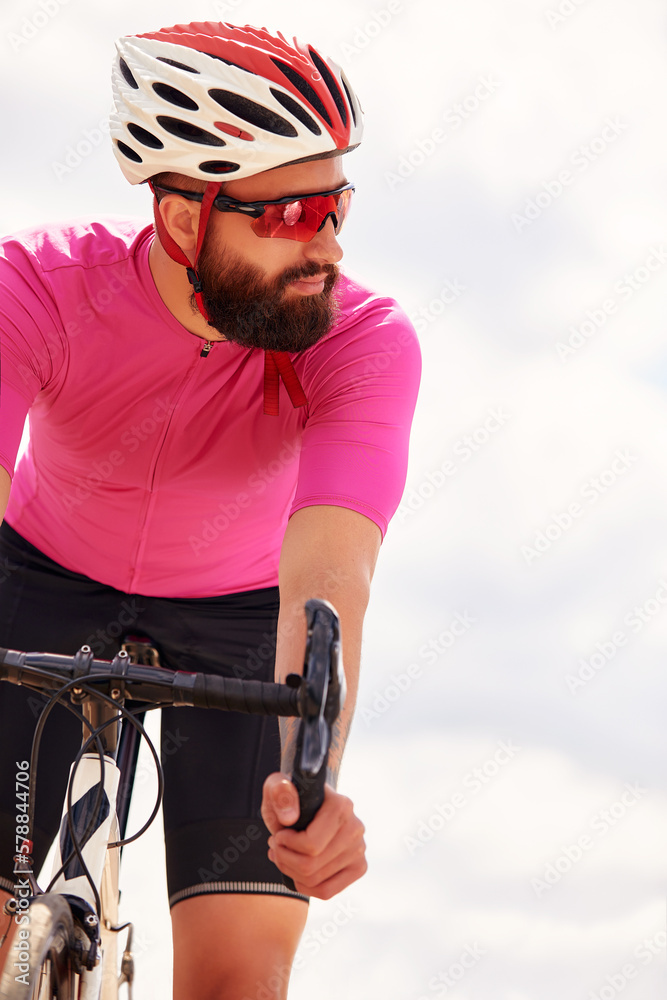 Naklejka premium Portrait of a professional cyclist in sportswear, a protective helmet and goggles in a pink jersey against the blue sky, copies. The concept of an active and healthy lifestyle.