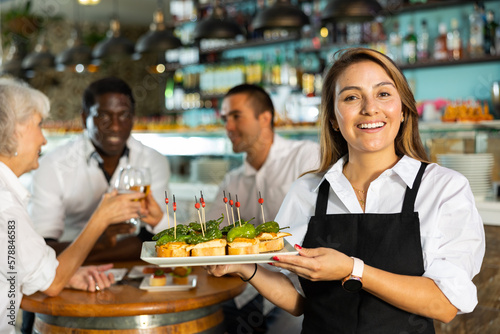 Positive female waiter holding tray with pinchos at restaurant