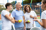 Portrait of four tennis players of different ages standing with padel rackets and balls outdoors on sunny day