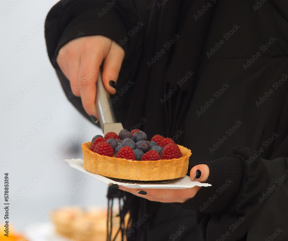 Closeup of a vendor at a pastry stand scooping a tart onto a paper tray at Prague farmers street food market in cold winter day.