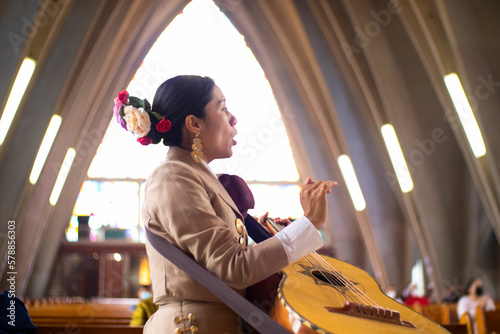 beautiful hispanic singer mariachi woman playing mexican big guitar or guitarron and singing, mexican mariachi music played in a church by women in mexico photo