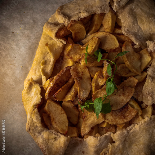 Rustic apple galette on parchment paper garnished with a sprig of mint.