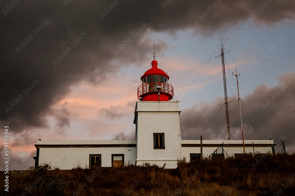 The classic lighthouse with red head during the sunset, dramatic clouds in the sky.