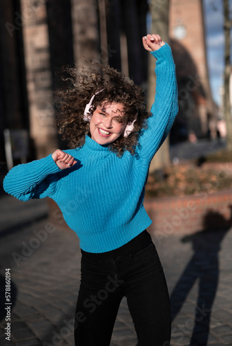 Beautiful curly haired young woman with headphones dancing outdoors.