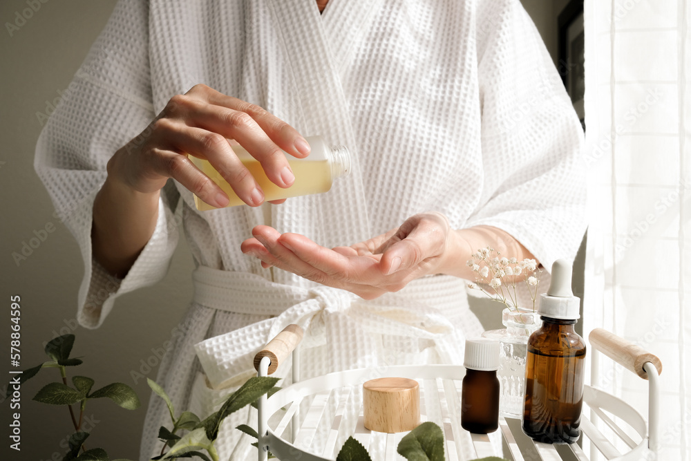 The woman wearing a bathrobe pours oil on her skin. Skincare and spa concept. the beauty care and wellness lifestyle. - obrazy, fototapety, plakaty 