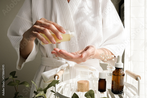 The woman wearing a bathrobe pours oil on her skin. Skincare and spa concept. the beauty care and wellness lifestyle.