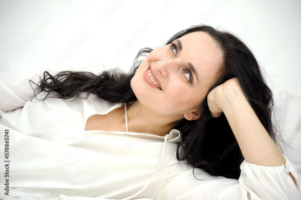 Fototapeta premium very beautiful middle-aged woman lying on the bed adjusting her hair white nightgown nightgown blue eyes black hair red nails manicure personal care Tenderness trying to lie down comfortably