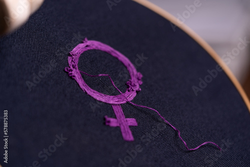 detalle de símbolo feminista bordado recién terminado con hilo suelto, sobre bastidor redondo de madera