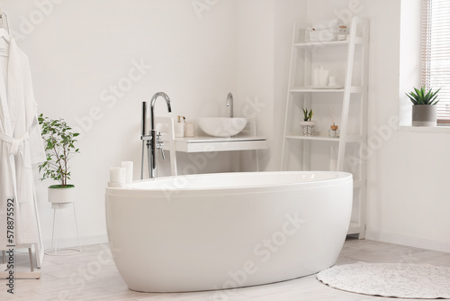 Interior of light bathroom with bathtub  sink and shelving unit