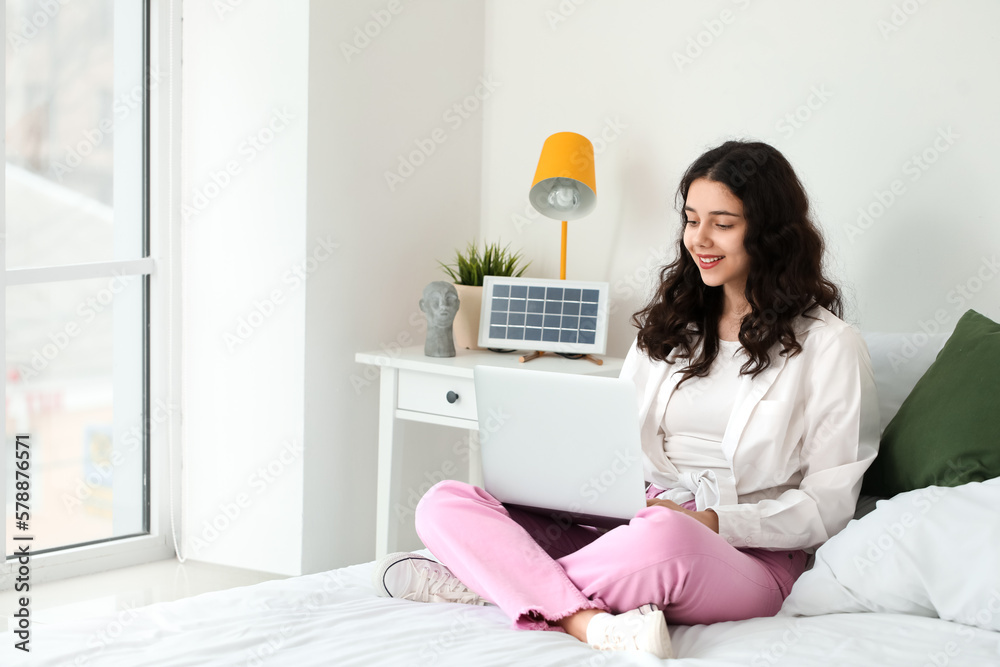 Teenage girl using laptop near portable solar panel in bedroom Teenage girl using laptop near portable solar panel in bedroom