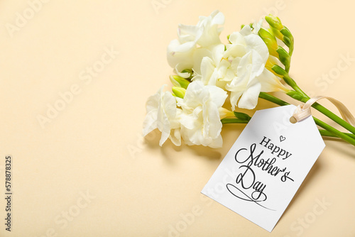 Greeting card with text HAPPY MOTHER'S DAY and beautiful freesia flowers on beige background