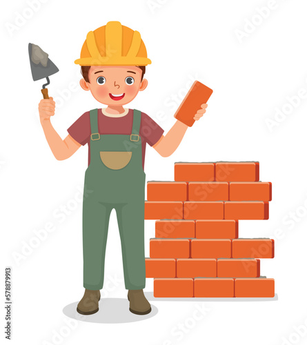 Cute little boy builder holding cement bricklayer tool working at the construction site