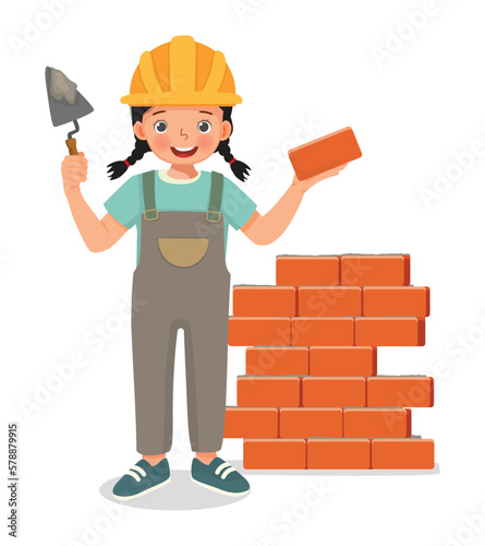 Cute little girl builder holding cement bricklayer tool working at the construction site