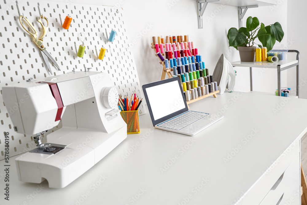 Tailor's workplace with laptop, sewing machine and thread spools in ...