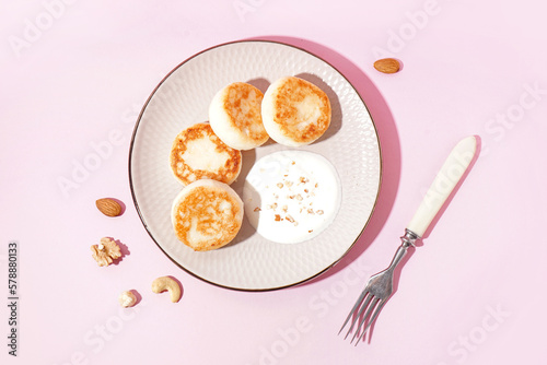 Plate with tasty cottage cheese pancakes and sour cream on pink background photo