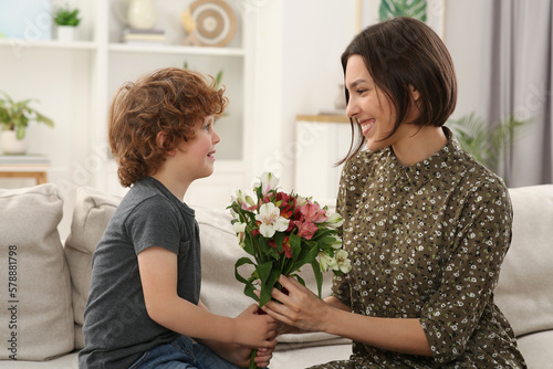 Happy woman with her cute son and bouquet of beautiful flowers at home. Mother's day celebration