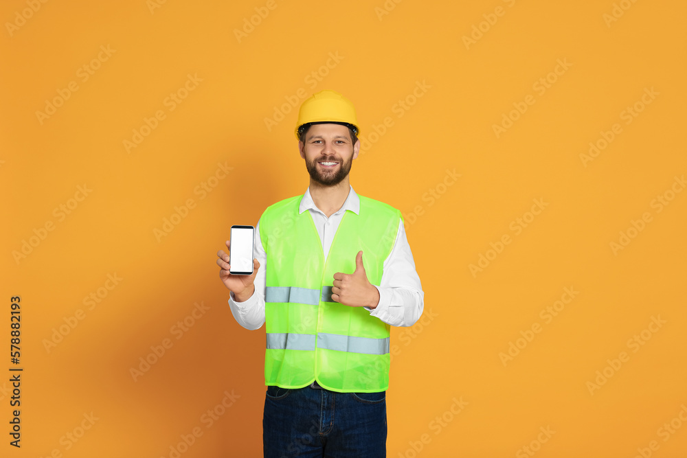 Man in reflective uniform showing smartphone and thumbs up on orange background