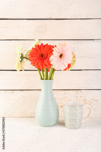 Vase with beautiful gerbera flower on table near white wooden wall