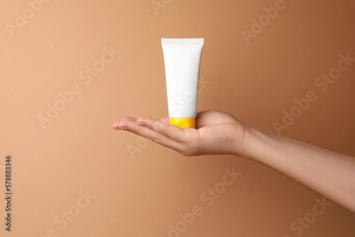 Woman holding tube of face cream on beige background, closeup. Space for text © New Africa