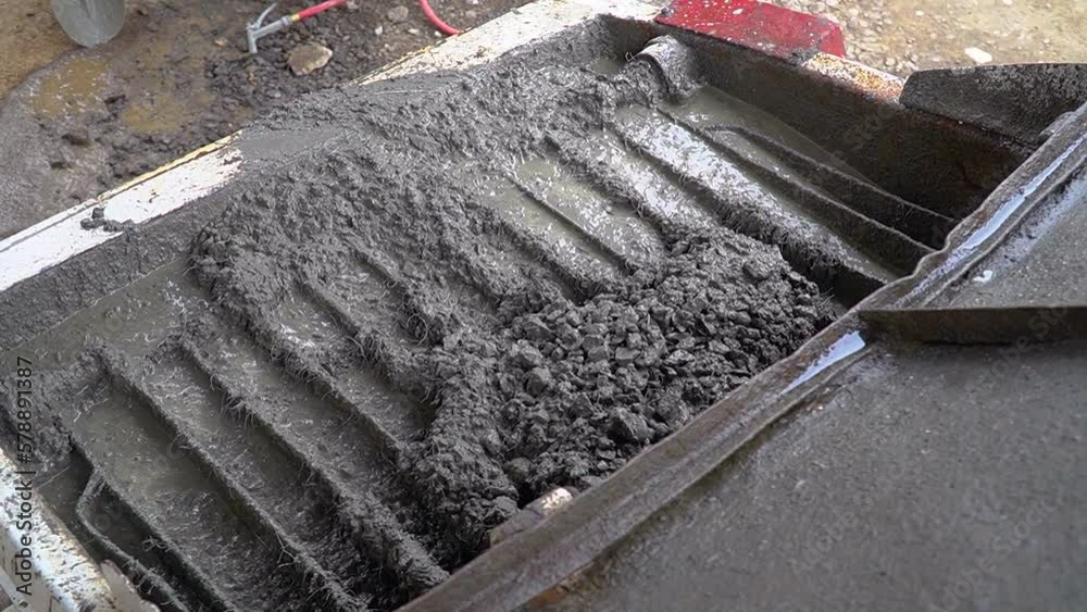 Fluid concrete mix and pebbles poured into a formwork at a construction site. Handheld closeup shot.
