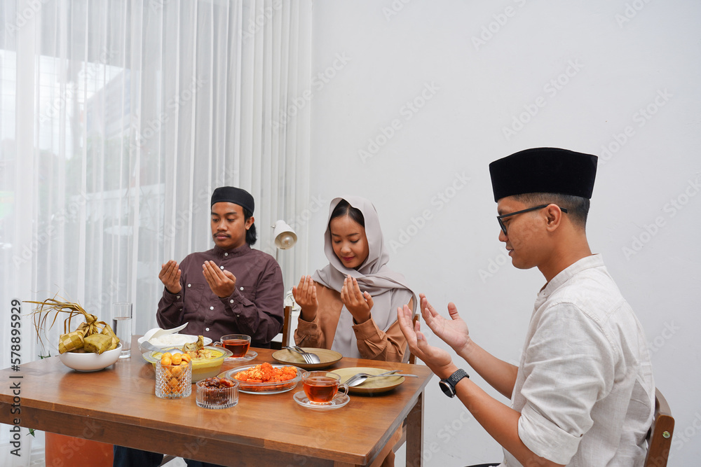 Asian Muslim family praying before having Iftar dinner. Eating traditional Indonesian food during Ramadan feasting month at home. Asian Muslim family praying before having Iftar dinner. Eating traditional Indonesian food during Ramadan feasting month at home.