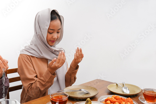 Asian Muslim woman praying before having Iftar dinner. Eating traditional Indonesian food during Ramadan feasting month at home.  photo