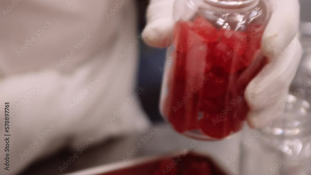 Red gummy multivitamins manually bottled by gloved hands; close-up