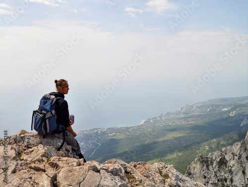 On a top of Ai-Petri. There is a man sittin on the edge of the rock. There is a city and Black sea on the background.