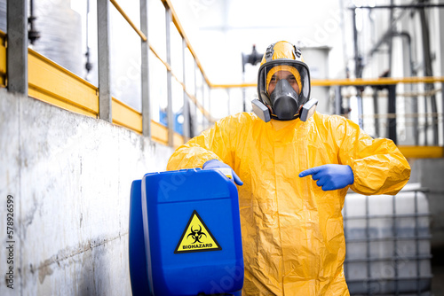 Portrait of worker wearing protection equipment and gas mask working in chemicals production factory pointing finger to biohazard waste.