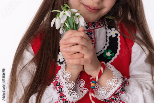 Bulgarian girl in traditional folklore costumes with spring flowers snowdrop and handcraft wool bracelet martenitsa symbol of Baba Marta