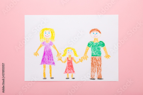 Drawn father, mother and daughter shapes with colorful wax crayons on white paper sheet on light pink table background. Pastel color. Closeup. Happy loving family concept. Top down view.