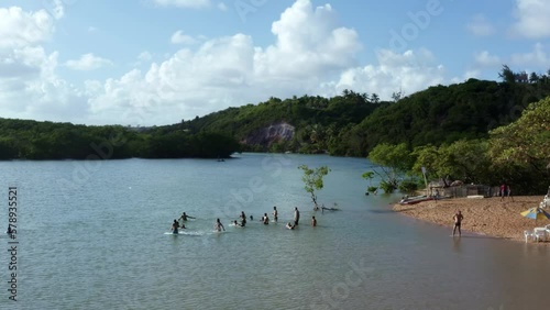 Dolly in aerial drone shot passing over a small group of people playing in the water of the winding large tropical Gramame river near the tropical beach capital city of Joao Pessoa in Paraiba, Brazil. photo