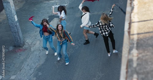 Delighted schoolgirls classmates standing on street dancing singing having fun near dance studio rehearsal time outside performers show motions movements skills .