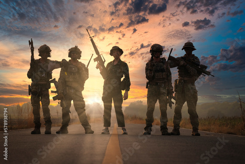 Five soldiers are standing lined up on the road during sunset after completing a combat mission