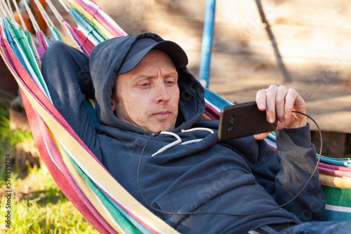 Pensive man on rainbow hammock watching by phone