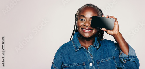 Cheerful woman with dreadlocks smiling and holding a smartphone