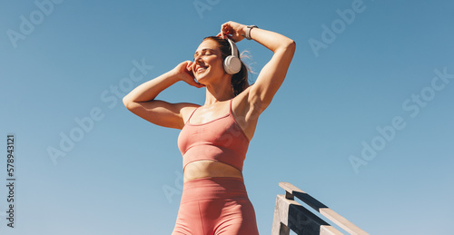 Fototapeta Caucasian sports woman listening to music on headphones outdoors