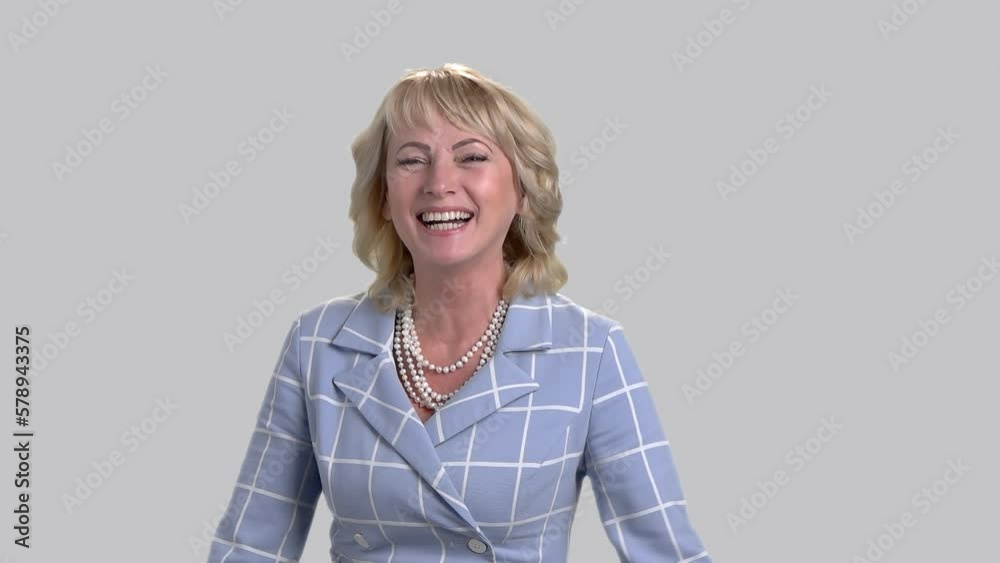 Mature woman in business suit laughing hard isolated on grey. Slow motion. Middle aged woman laughing out loud.