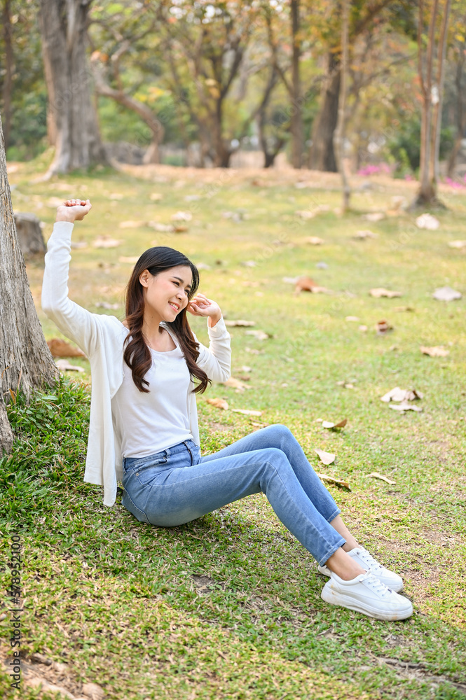 Carefree Asian woman stretched her arms while sitting on grass and relaxing in the green park. Carefree Asian woman stretched her arms while sitting on grass and relaxing in the green park.