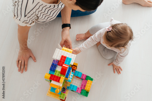 young nanny and adorable child playing with multicolored building blocks on floor photo