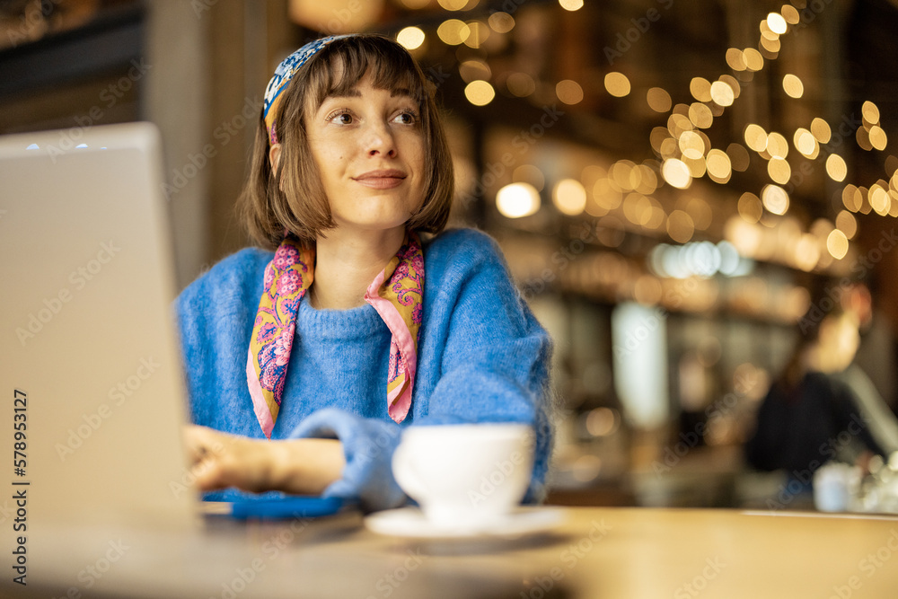 Young stylish woman works on laptop while sitting with a coffee drink at modern cafe. Concept of remote work from public place, digital freelance and modern lifestyle Young stylish woman works on laptop while sitting with a coffee drink at modern cafe. Concept of remote work from public place, digital freelance and modern lifestyle