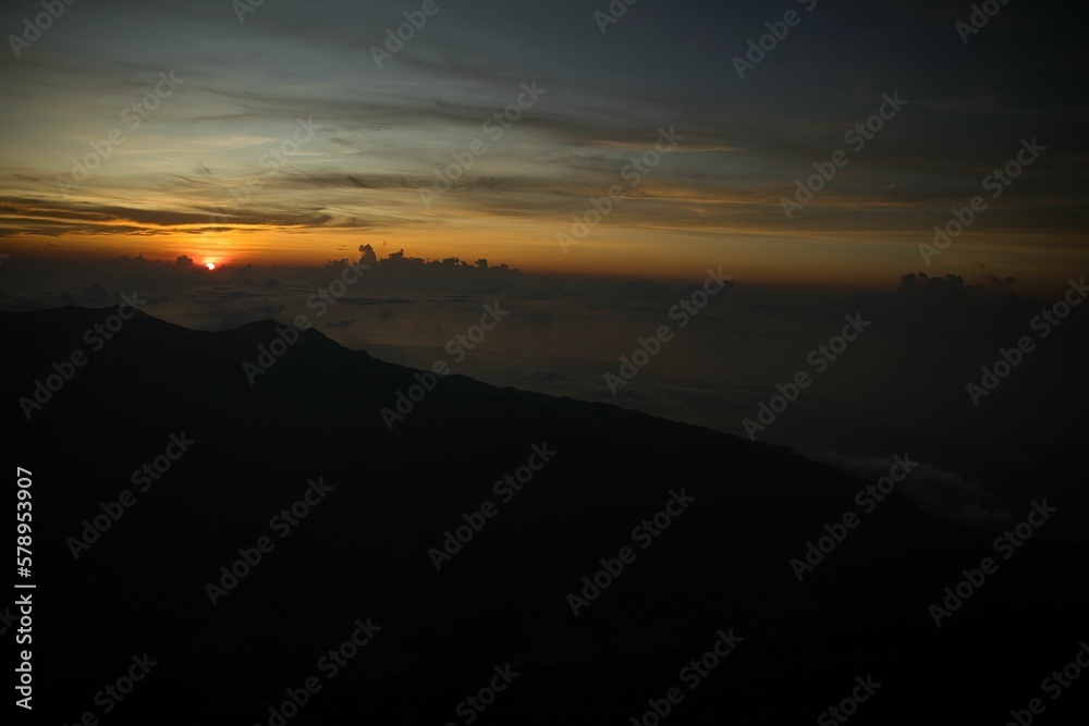 Sunrise on the top of the mountain Inerie on Flores, the sun is just about to rise in red yellow golden colors across the still dark sky.